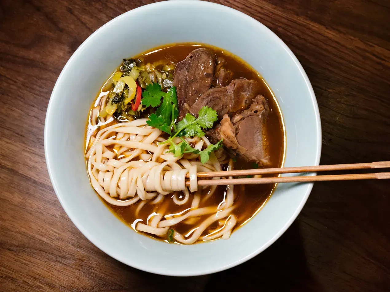 Bowl of beef noodle soup with chopsticks.