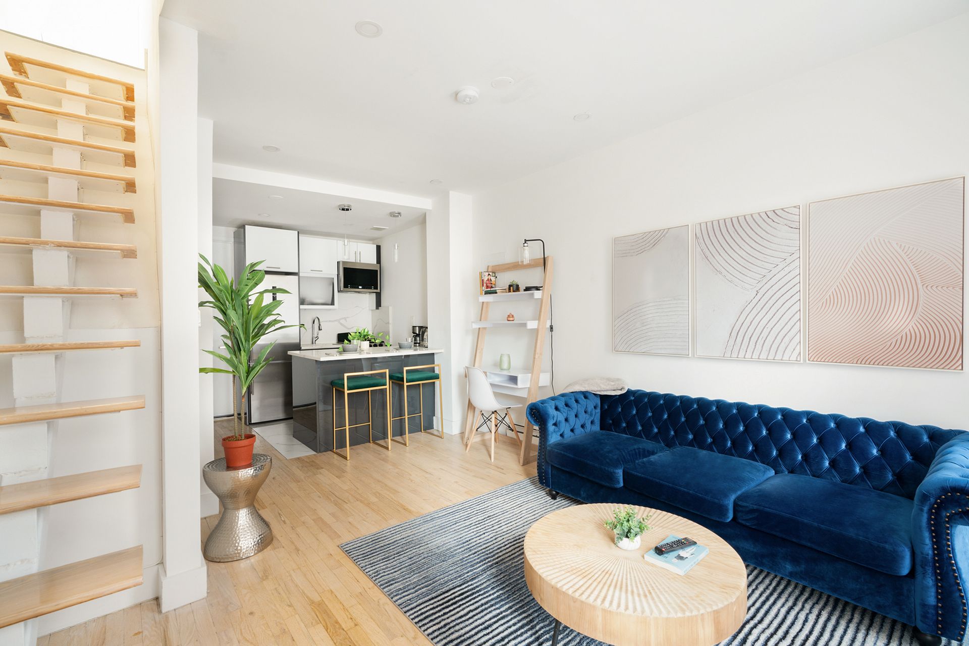 Living room with blue sofa, kitchen, open stairs, and artwork.