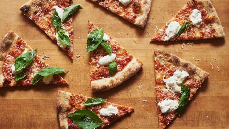 Triangular pizza slices with red sauce, cheese, and basil leaves on a wooden surface.