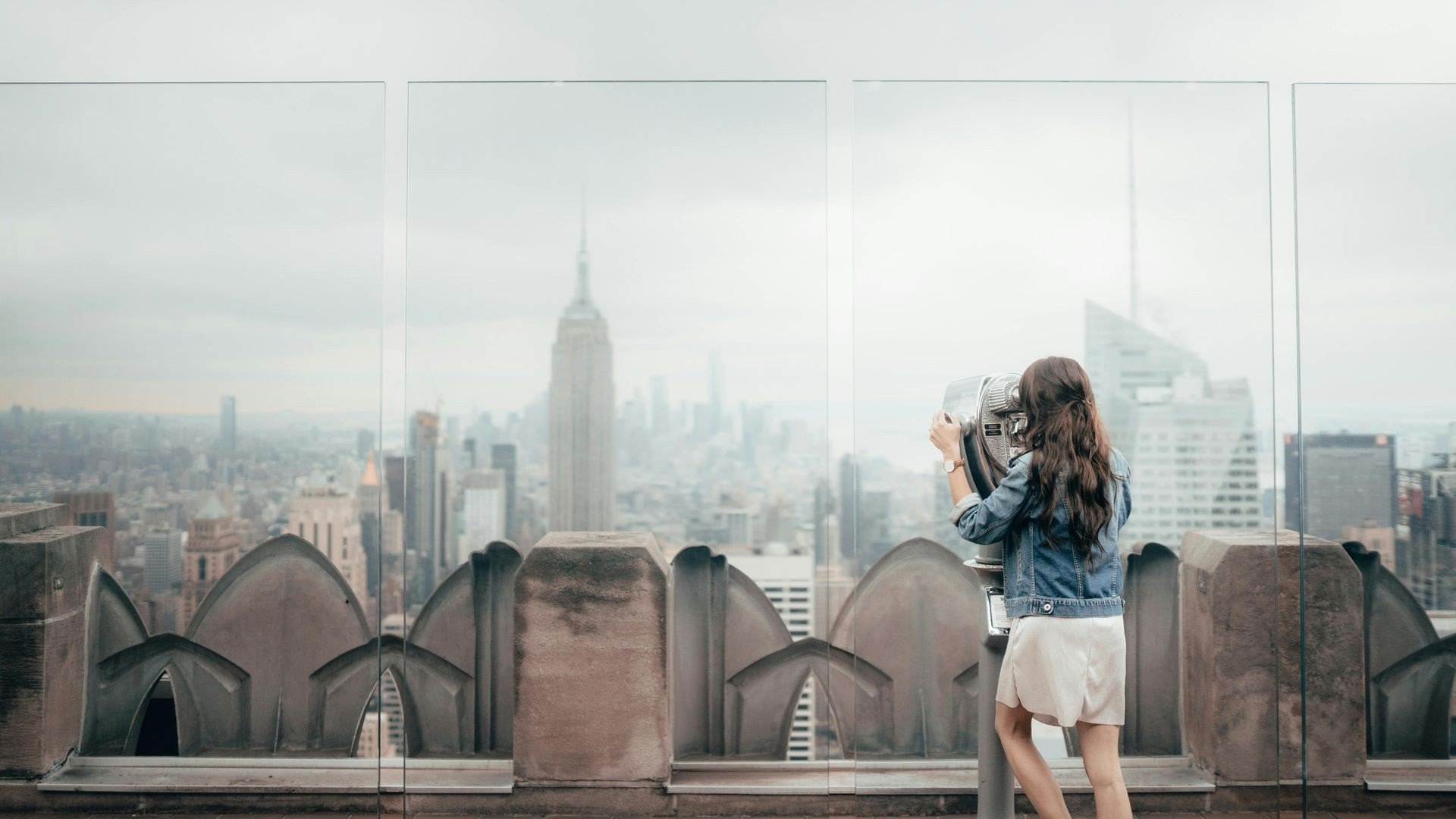 Woman looking at the New York City skyline through binoculars from a rooftop viewpoint