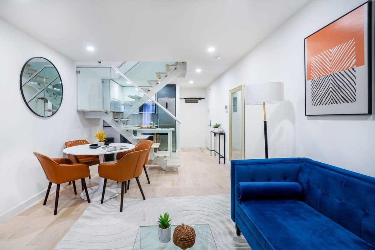 Modern living room with a blue sofa, dining area, and a staircase.