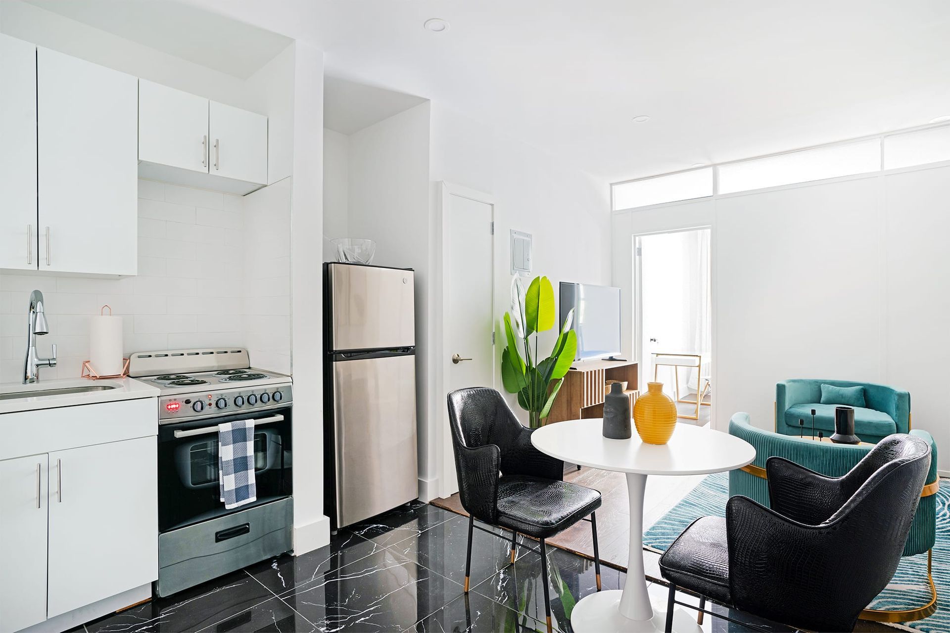 Bright, modern apartment interior. Kitchen with stainless steel appliances, dining area, and teal seating.