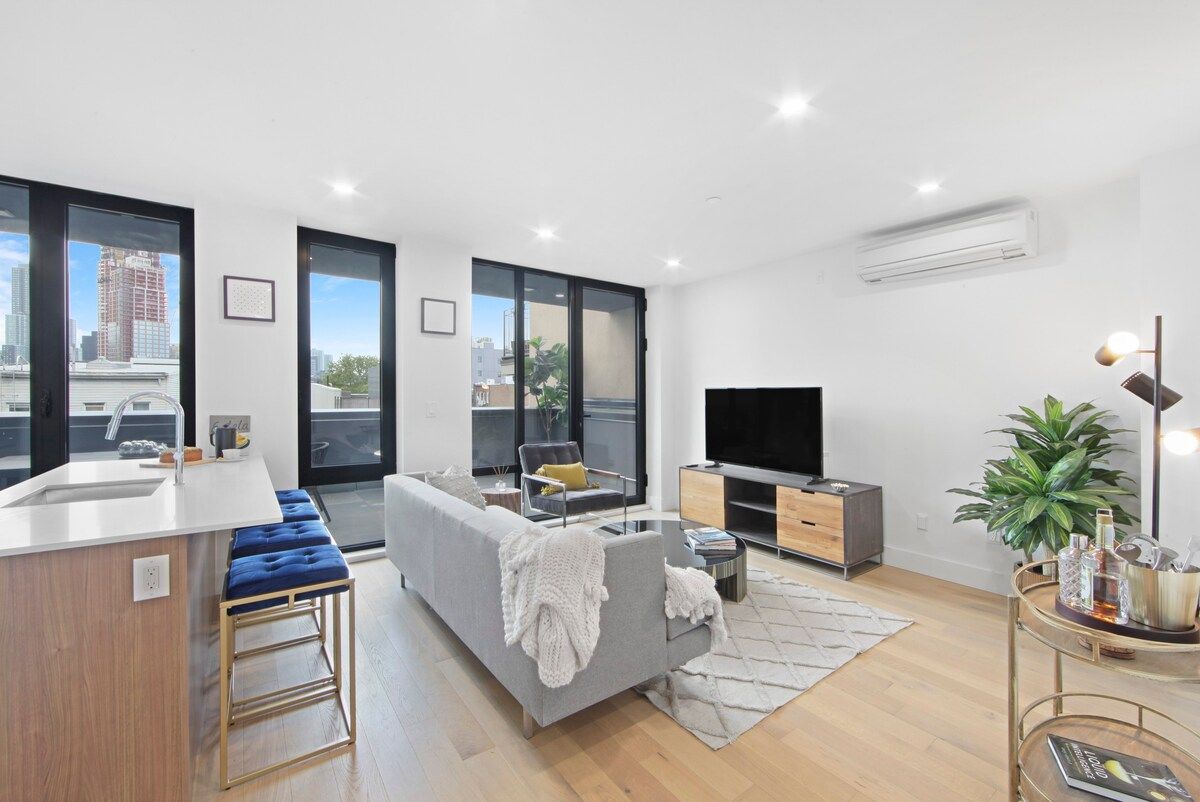 Modern living room with a gray sofa, TV, and large windows.