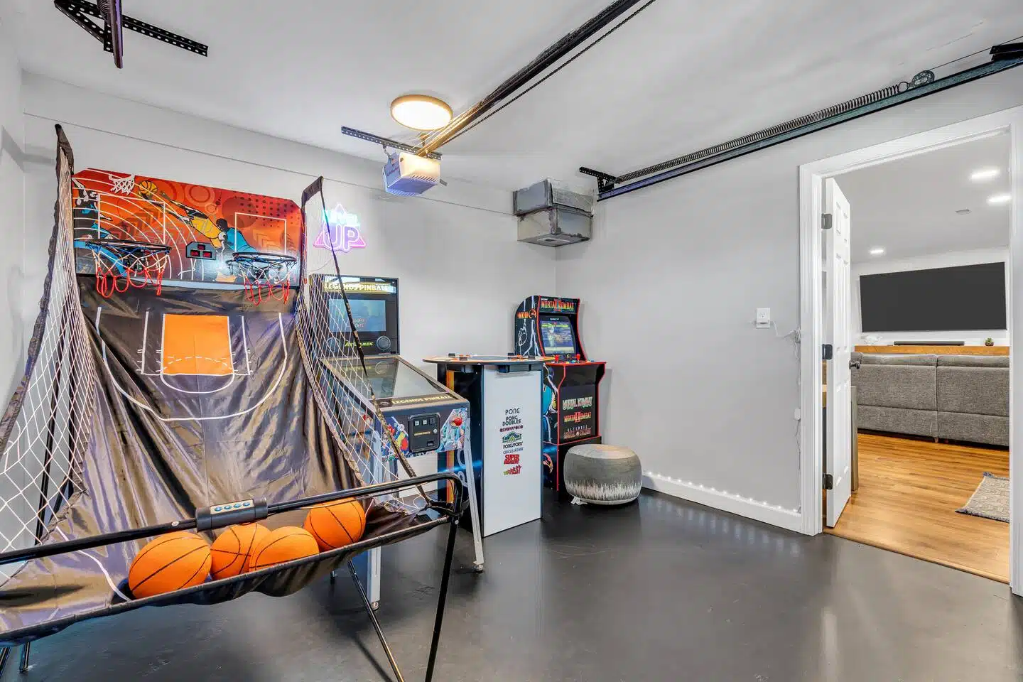 Indoor game room featuring a basketball arcade game with basketballs, retro arcade machines, and a cozy seating area, ideal for vacation rentals at the Jersey Shore.