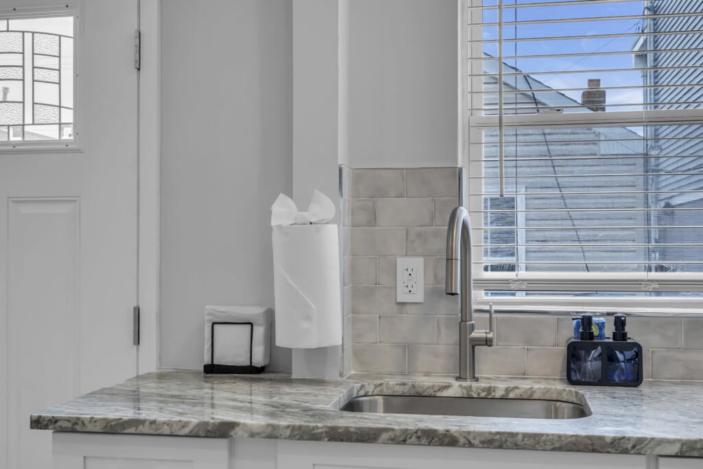 Modern kitchen sink area with granite countertop, paper towel holder, and window view, emphasizing cleanliness and maintenance for vacation rental properties.