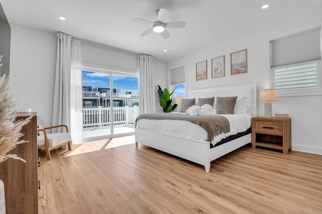 Bright and airy beach rental bedroom with large window, wooden flooring, white bedding, and coastal decor, ideal for vacationers seeking relaxation at the Jersey Shore.