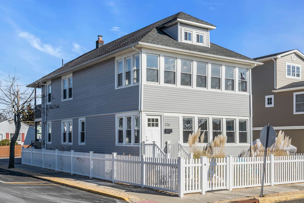 Coastal vacation home in Jersey Shore, featuring a modern exterior, white picket fence, and nearby amenities, representing investment potential and lifestyle benefits.