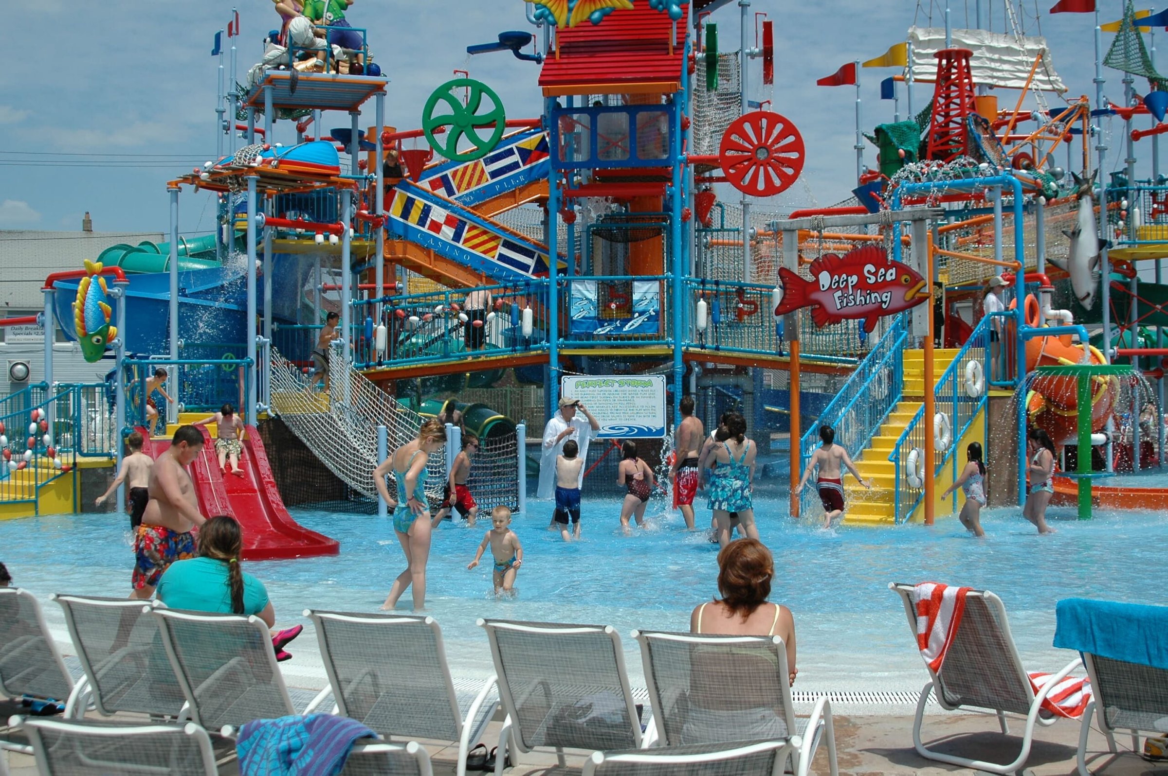 Colorful water play area at Breakwater Beach waterpark, featuring children enjoying slides and water attractions, surrounded by lounge chairs for relaxing visitors.