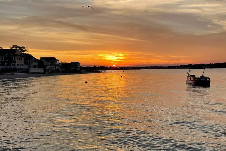 Sunset over Toms River with calm waters, a small boat, and beach houses reflecting the tranquil atmosphere of Ocean Gate, a peaceful Jersey Shore community.