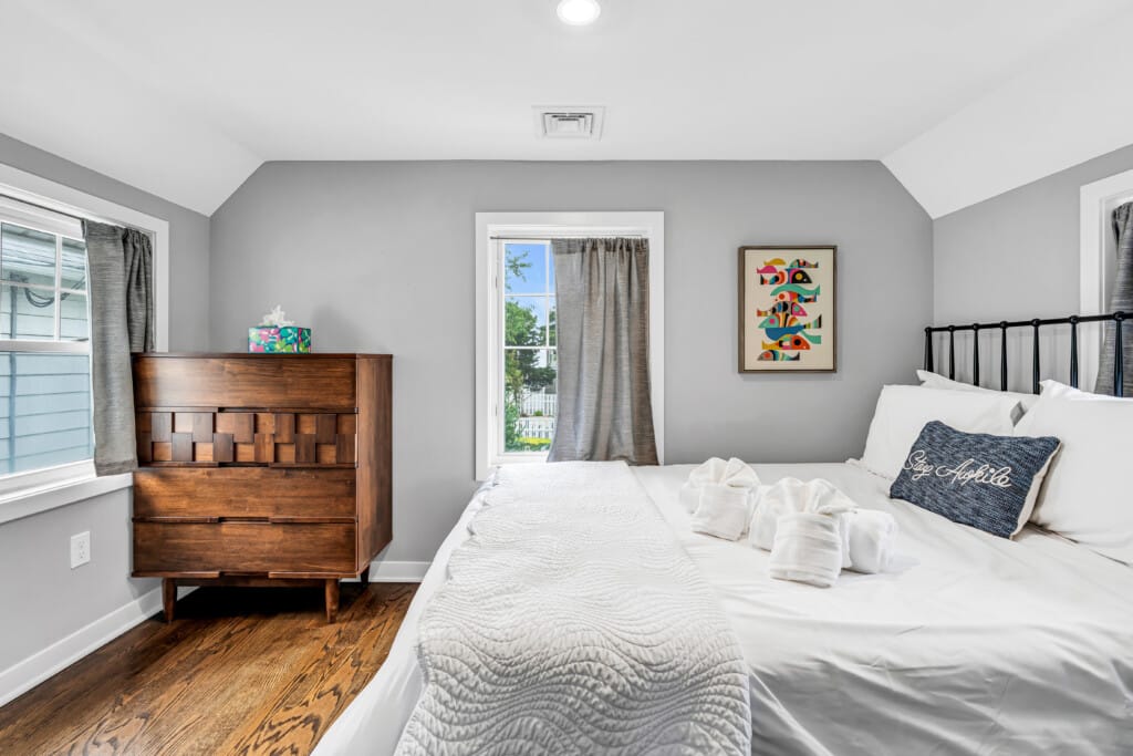 Cozy bedroom featuring a wooden dresser, decorative wall art, and neatly arranged towels on a bed, emphasizing the inviting atmosphere of Jersey Shore vacation homes.