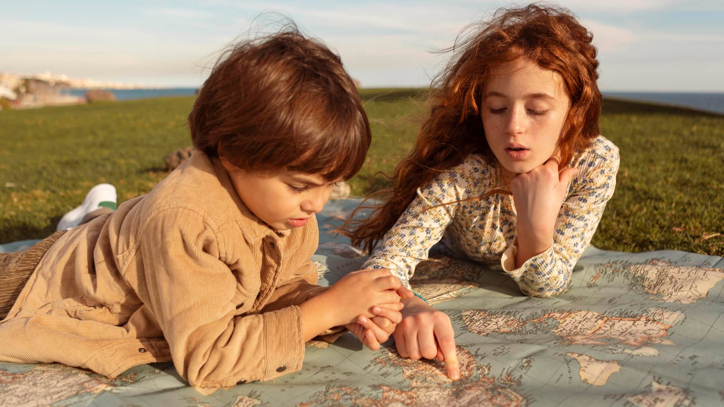 Kids exploring a map on grass, highlighting travel planning and exploration for Jersey Shore vacations.