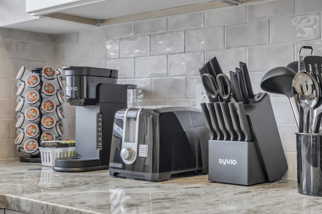 Modern kitchen countertop featuring a coffee maker, toaster, knife block, and utensils, highlighting functional and stylish appliances for vacation rentals.