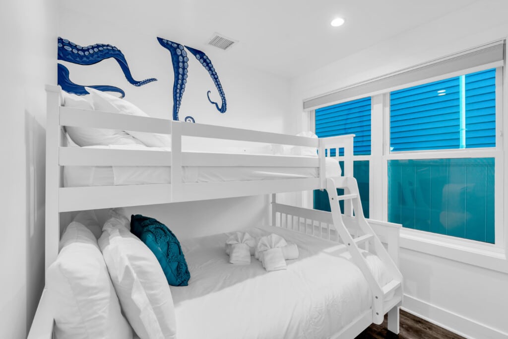 Bunk bed in a coastal-themed bedroom with blue octopus mural, bright white linens, and turquoise accents, highlighting vacation rental appeal at the Jersey Shore.