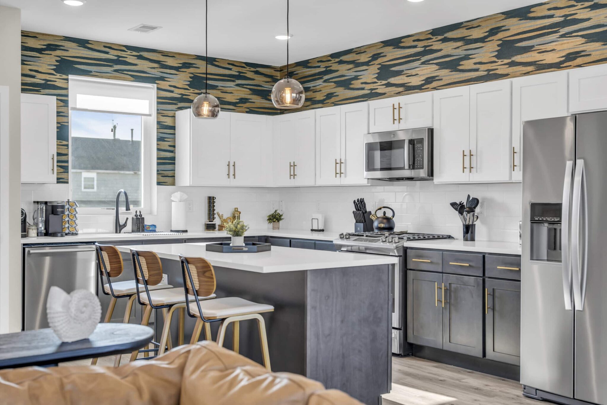 Modern kitchen with white cabinetry, stainless steel appliances, and stylish blue and wood-patterned accent wall, featuring seating at the island, ideal for Jersey Shore vacation rentals.