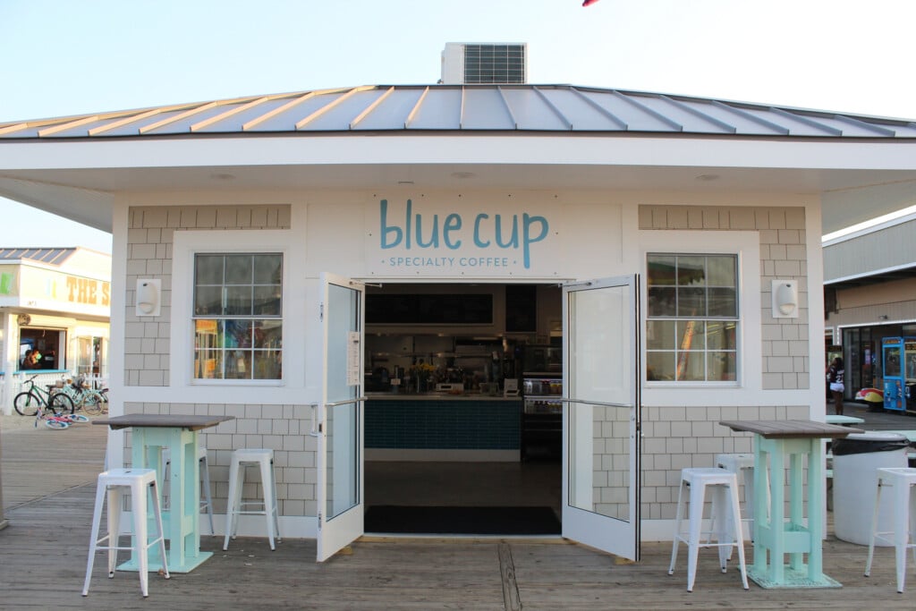Blue Cup Coffee shop exterior on Seaside Park Boardwalk, featuring open doors, light blue signage, and outdoor seating, highlighting its beachside coffee offerings.