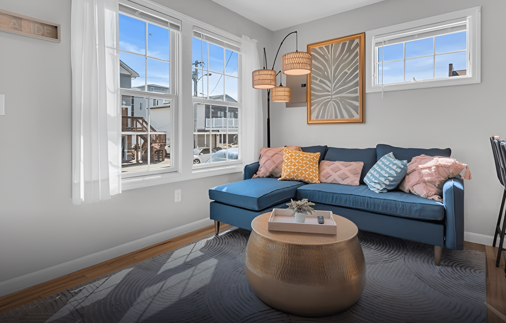 Cozy beach rental living room with blue sectional sofa, decorative pillows, round gold coffee table, and large windows showcasing outdoor views, ideal for vacation planning at the Jersey Shore.