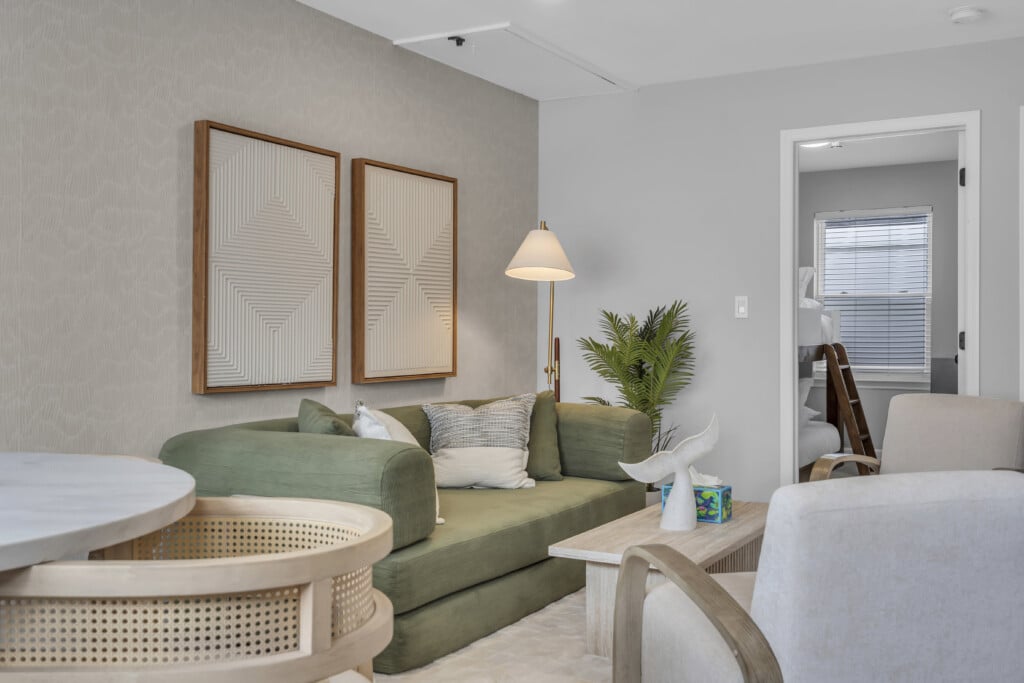 Modern vacation rental living room featuring a green sofa, decorative wall art, a stylish lamp, and a dining table, emphasizing comfort and aesthetic appeal for potential guests.
