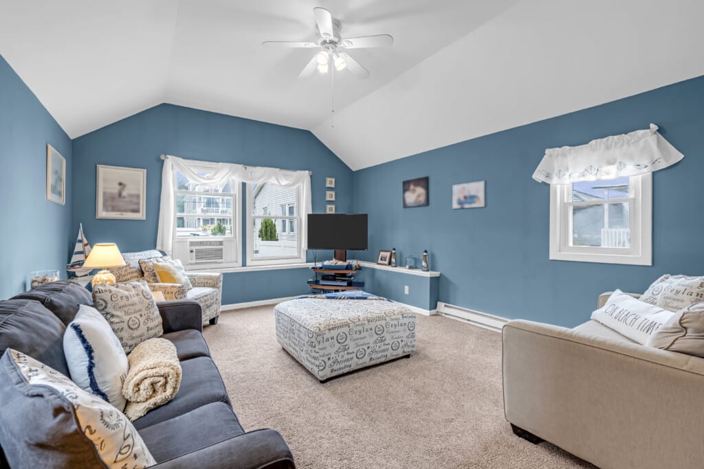 Cozy living room in a shore property, featuring blue walls, comfortable seating, an entertainment center, and large windows letting in natural light, ideal for showcasing beach house aesthetics.