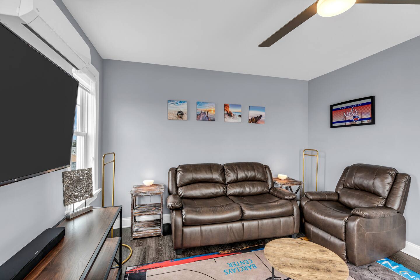 Cozy living room with leather sofas, wall-mounted TV, and Jersey Shore-themed artwork, showcasing Breezy Beach Stays’ vacation rental ambiance.