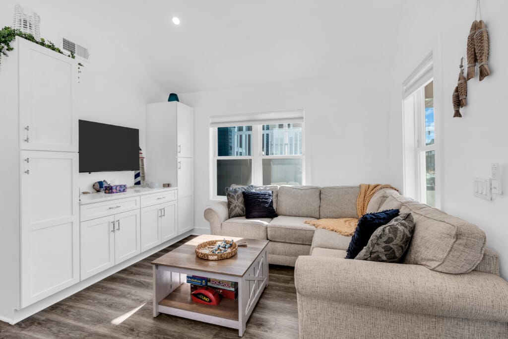 Cozy beach house living room featuring a light-colored sectional sofa, wooden coffee table with games, and bright coastal decor, ideal for showcasing shore property staging and preparation.