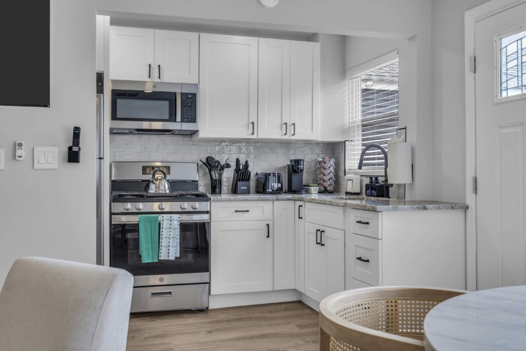 Modern kitchen with stainless steel appliances, including a gas stove and microwave, white cabinetry, and a granite countertop, showcasing a teal dish towel and coffee maker, ideal for vacation home rentals at the Jersey Shore.