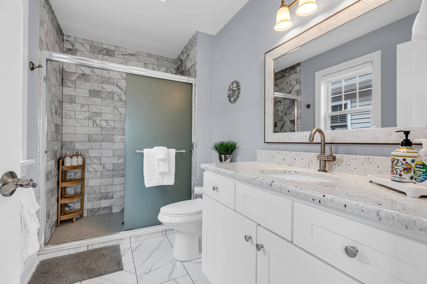 Modern bathroom with white cabinetry, marble countertop, glass shower enclosure, and decorative elements, illustrating the appeal of vacation rentals managed by Breezy Beach Stays at the Jersey Shore.