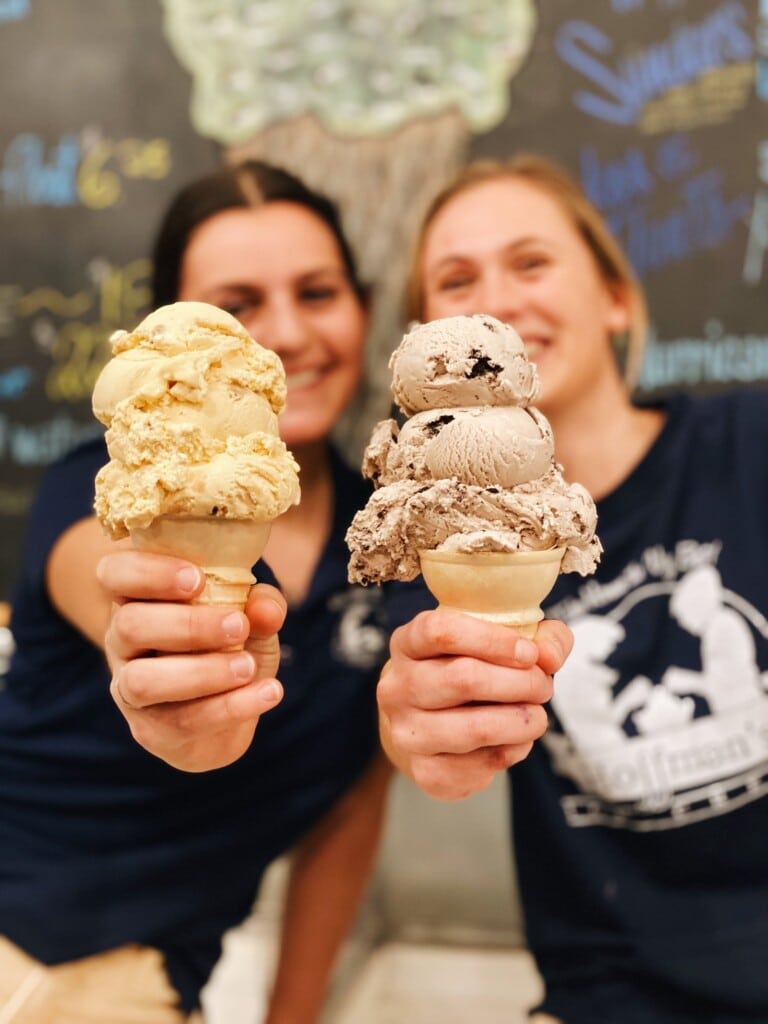Two women holding ice cream cones with scoops of creamy flavors, showcasing Hoffman’s Ice Cream & Yogurt's homemade ice cream in a vibrant shop setting, highlighting the Jersey Shore's ice cream culture.