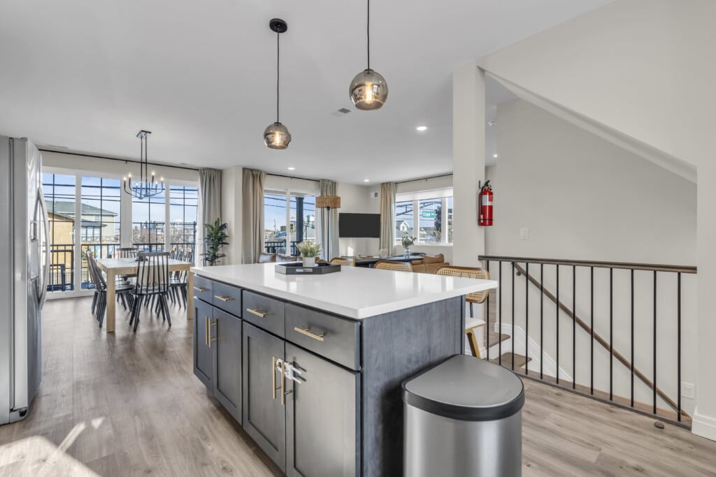 Modern kitchen and dining area in a vacation rental at the Jersey Shore, featuring a large island, stylish cabinetry, dining table with chairs, and large windows offering natural light and views.