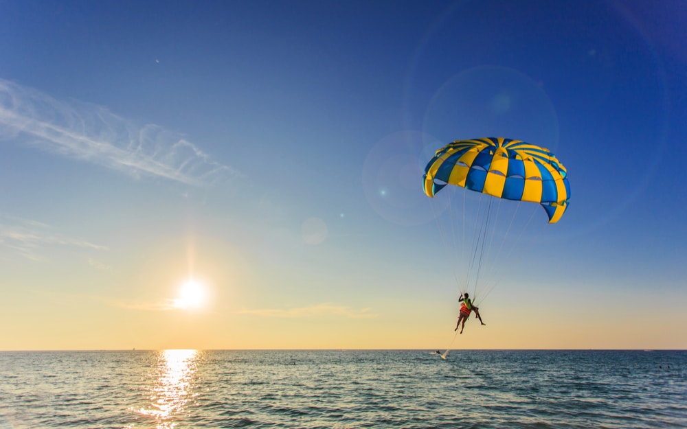 Parasailing experience over calm waters at sunset with colorful parachute and two participants, highlighting water sports activities near Seaside Heights, NJ.