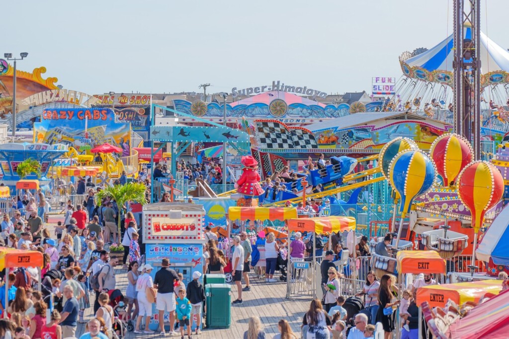 Crowded Jenkinson's Boardwalk amusement park featuring colorful rides, attractions, and food stalls, embodying family fun at the Jersey Shore.