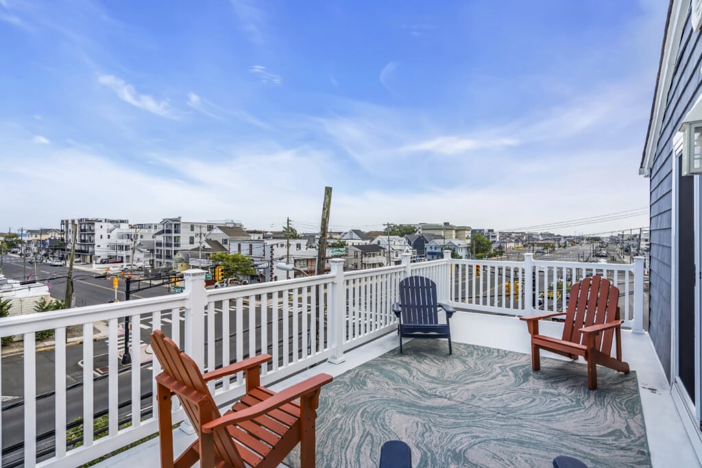 Rooftop deck with red and blue Adirondack chairs overlooking coastal homes and streets, emphasizing outdoor living and beachside relaxation.