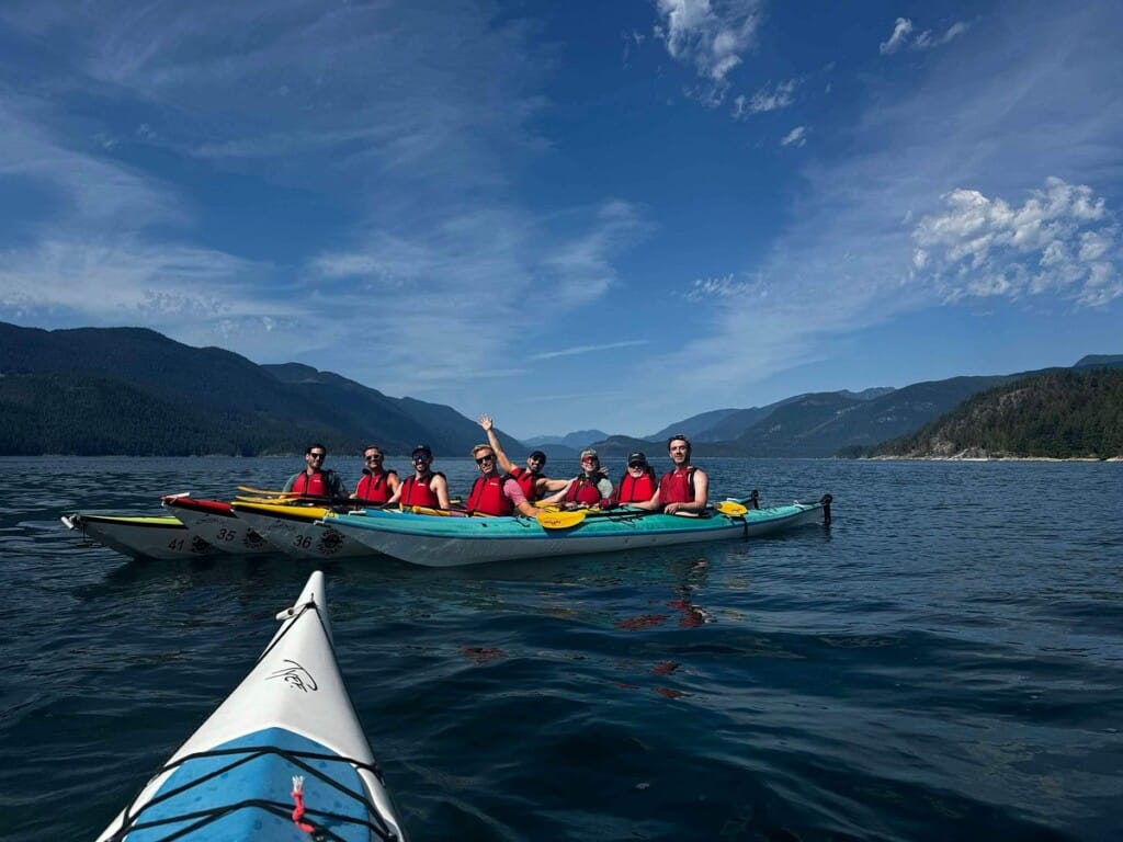 Group of kayakers in bright red life jackets enjoying a guided boat tour on calm waters, with mountains in the background, emphasizing family-friendly outdoor adventures and marine exploration.