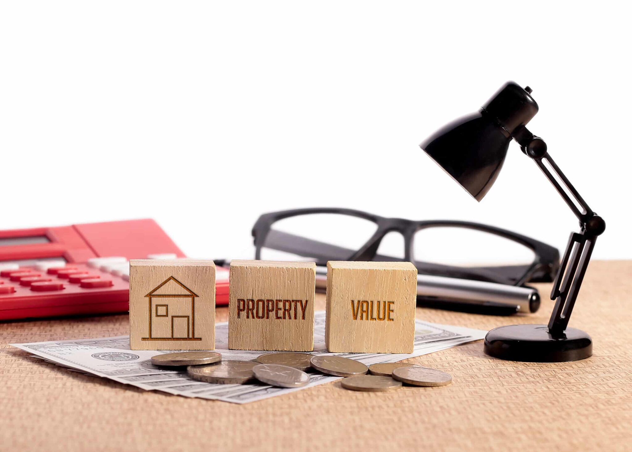 Close-up of wooden blocks labeled "PROPERTY" and "VALUE," a house icon, coins, a calculator, and a desk lamp on a white background, symbolizing shore home investment and upgrades for increased rental appeal.