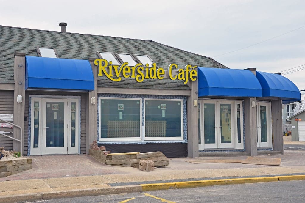 Riverside Café exterior with blue awnings, featuring dog-friendly outdoor seating near the Manasquan Inlet, ideal for enjoying meals with pets.
