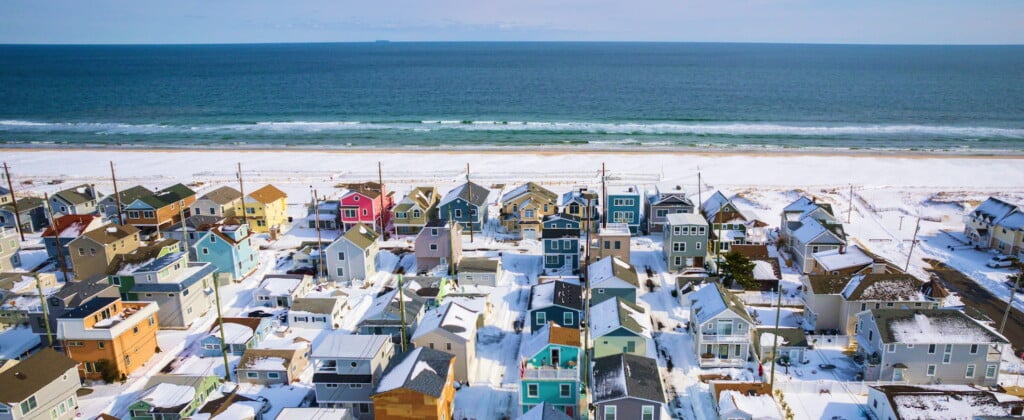 Aerial view of colorful beach houses in winter snow near the ocean, showcasing the charming coastal community of Ortley Beach and Lavallette, ideal for family-friendly vacations along the Jersey Shore.
