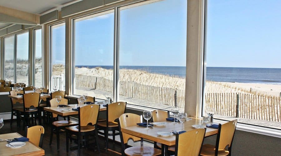 Elegant dining area at Chef Mike's ABG with panoramic ocean views, showcasing tables set for fine dining, large windows overlooking the Atlantic Ocean, and sandy beach dunes in the background.