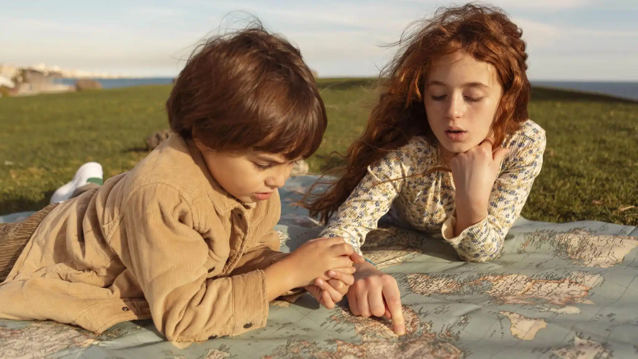 Kids exploring a map on a grassy area, engaged in planning adventures at the Jersey Shore, ideal for family getaways.