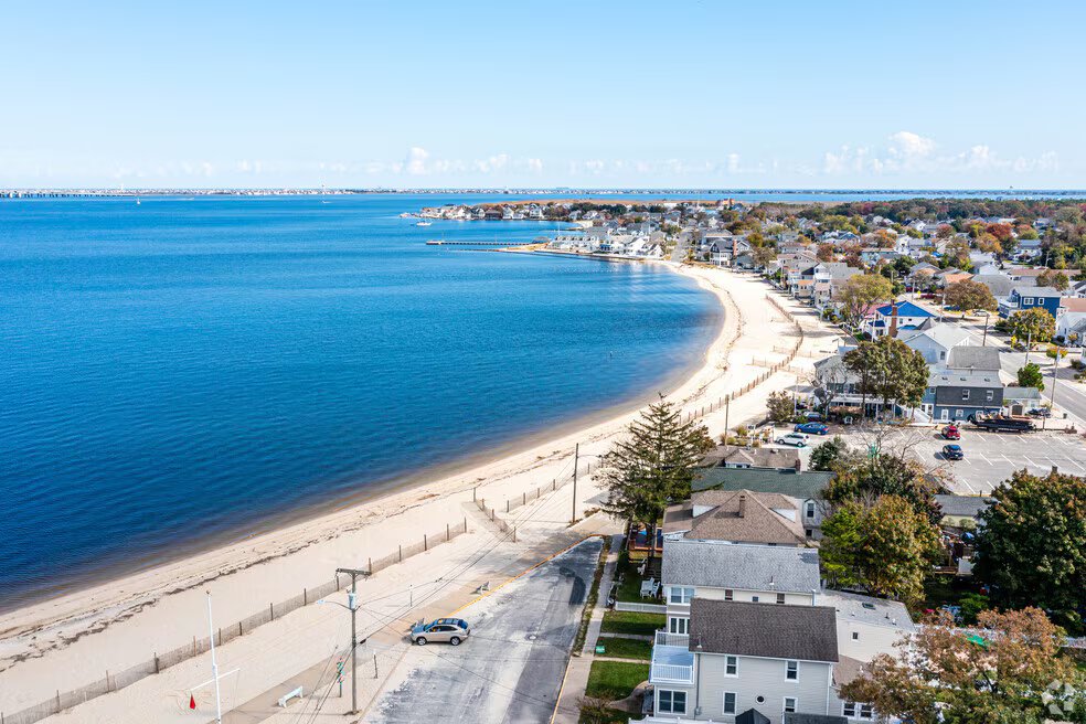 Aerial view of Ocean Gate, New Jersey, showcasing calm waters of Toms River, sandy beach, and nearby residential homes, emphasizing the area's charm and appeal for vacation rentals.