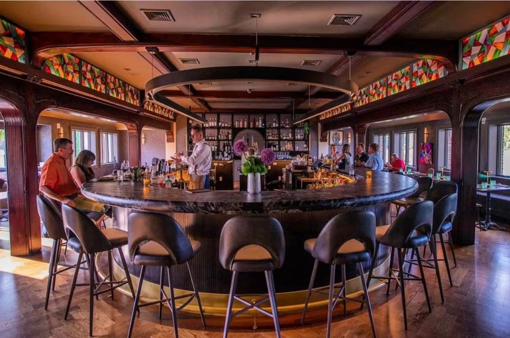 Elegant bar interior at Ember & Eagle featuring a circular counter, patrons enjoying drinks, and a warm, rustic-modern ambiance.