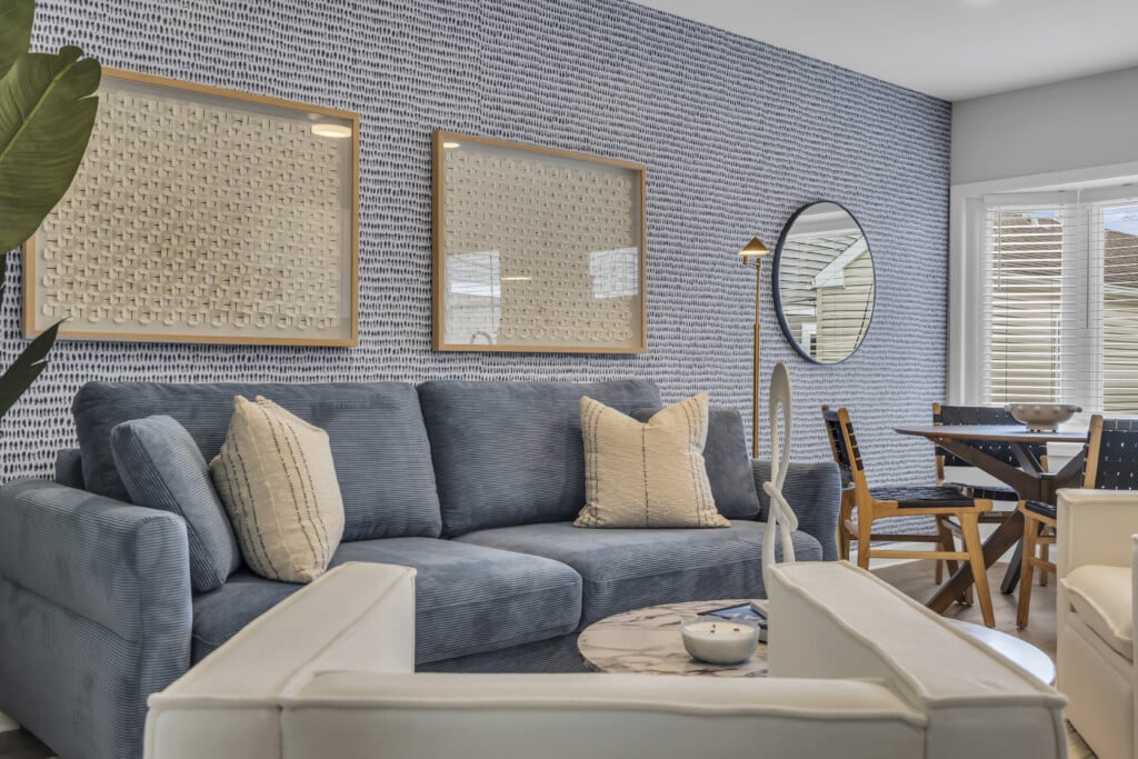 Cozy living room featuring a blue couch with decorative pillows, framed artwork on textured wall, round mirror, and dining table, showcasing a stylish Jersey Shore home interior ideal for vacation rentals.