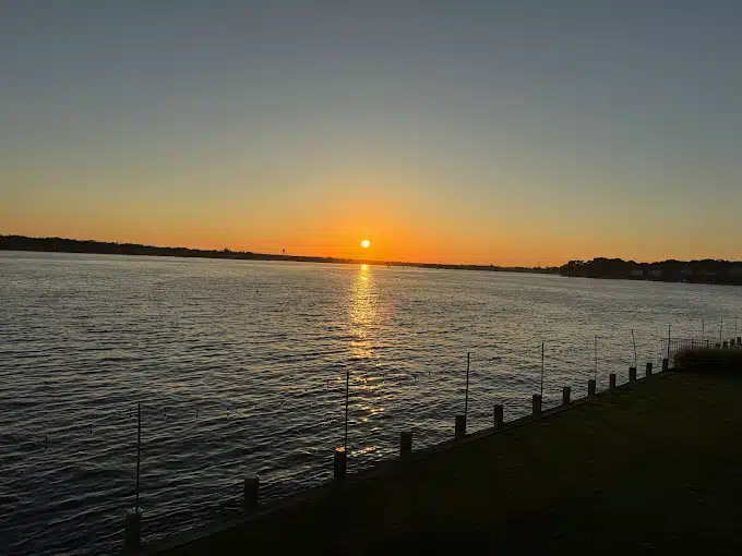 Sunset over Toms River, reflecting on calm waters, with silhouettes of shoreline and grass in foreground, highlighting the scenic beauty of the Jersey Shore near the Toms River Yacht Club.