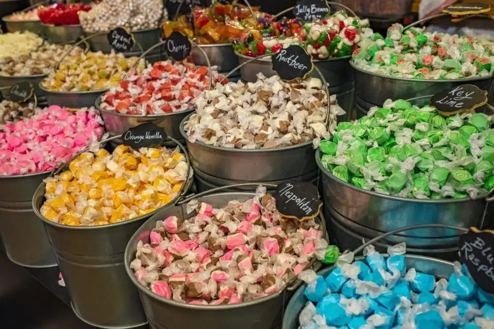 Colorful buckets of salt water taffy and candy varieties, showcasing iconic Jersey Shore treats, with labels for flavors like Key Lime, Neapolitan, and Orange Vanilla.