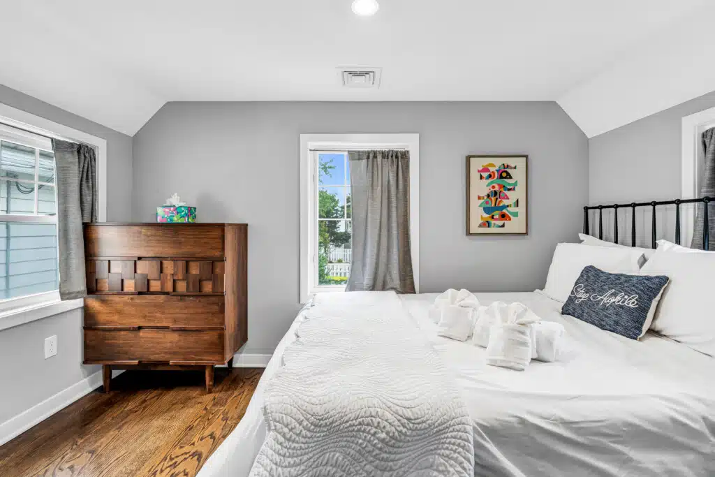 Cozy bedroom featuring a wooden dresser, decorative wall art, and neatly arranged towels on a bed, emphasizing the inviting atmosphere of Jersey Shore vacation homes.