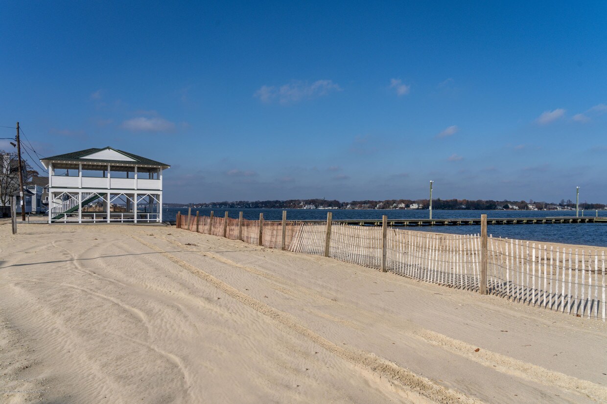 Beachfront view of a white building with green accents, sandy shore, and wooden pier in Ocean Gate, NJ, highlighting the area's tranquil atmosphere and vacation rental appeal.