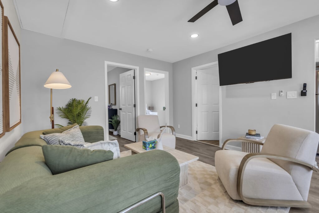 Cozy living room with green sectional sofa, modern decor, wall-mounted TV, and natural light, ideal for vacation rental management at Jersey Shore.