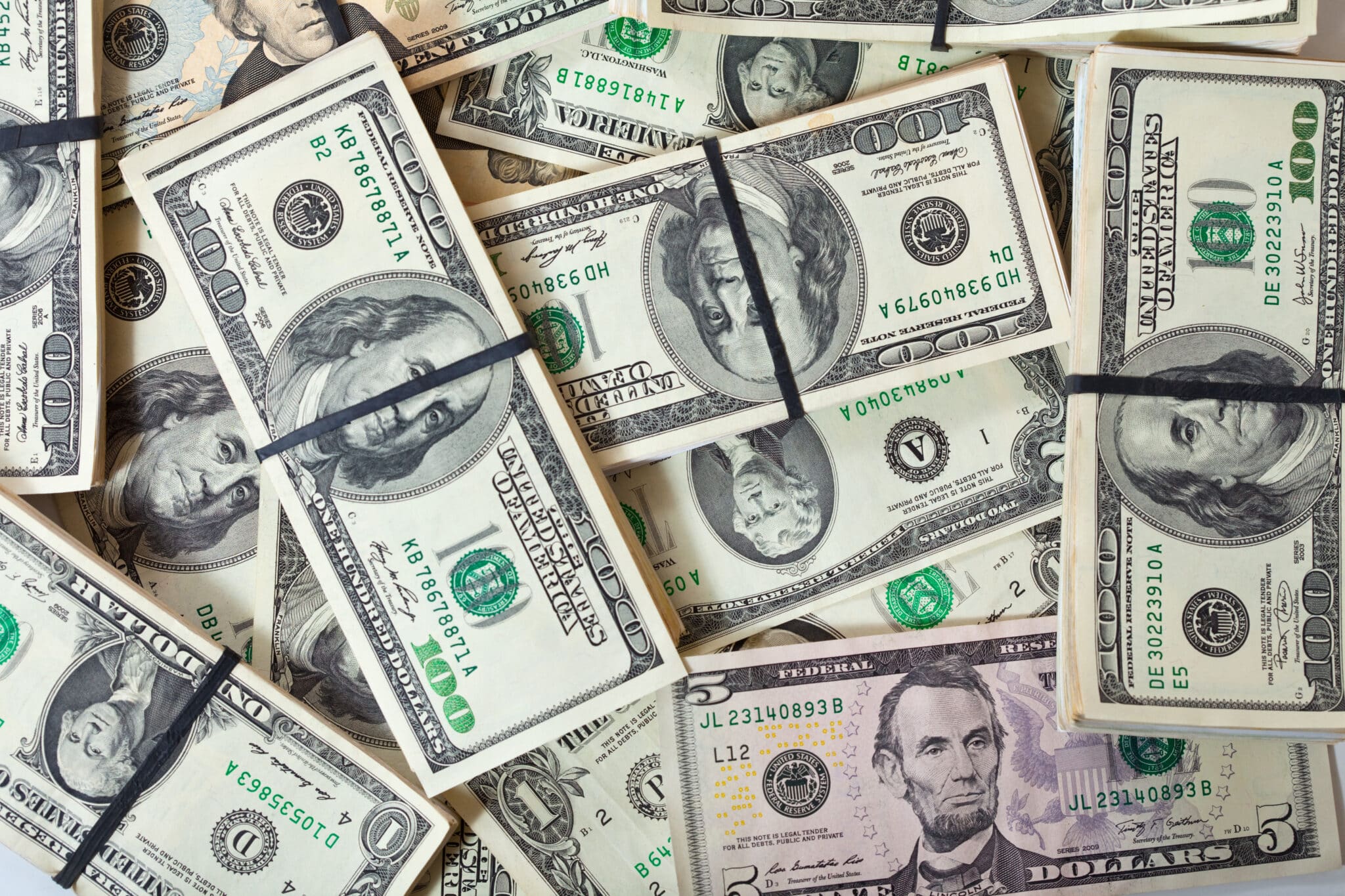 Stacks of U.S. dollar bills, including hundreds and fives, representing cash for beach tags, boardwalk games, and parking expenses during a Jersey Shore vacation.