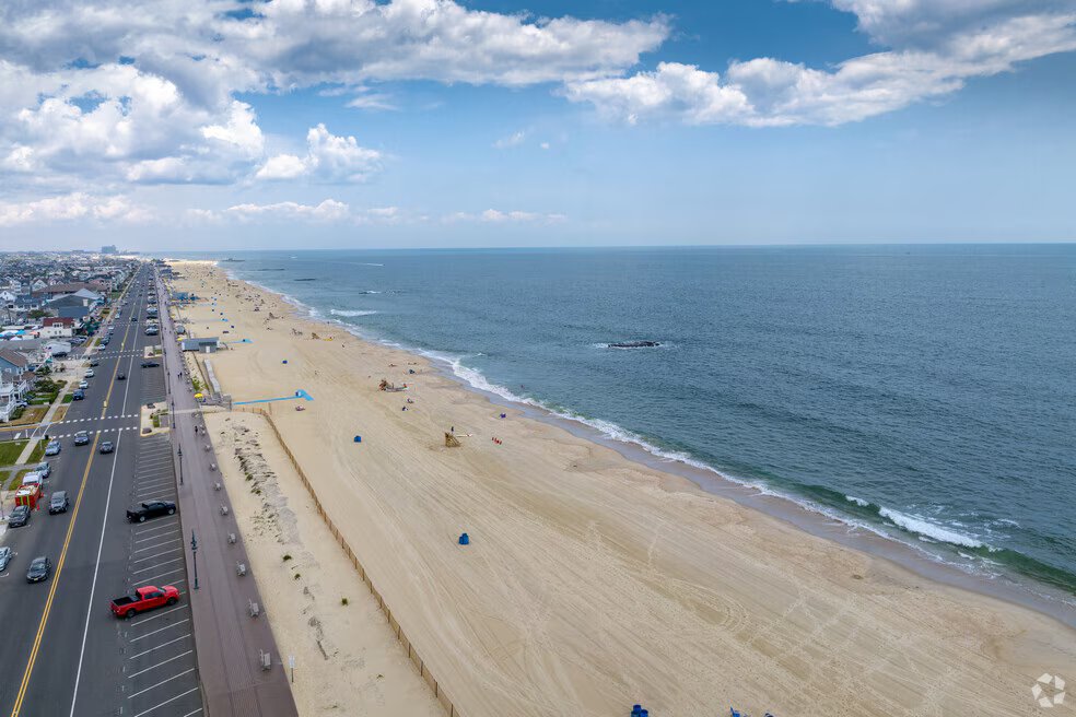 Aerial view of a sandy beach along the Jersey Shore, with minimal beachgoers, ocean waves, and a road lined with parked cars, illustrating the peaceful atmosphere of Lake Como for off-season vacations.