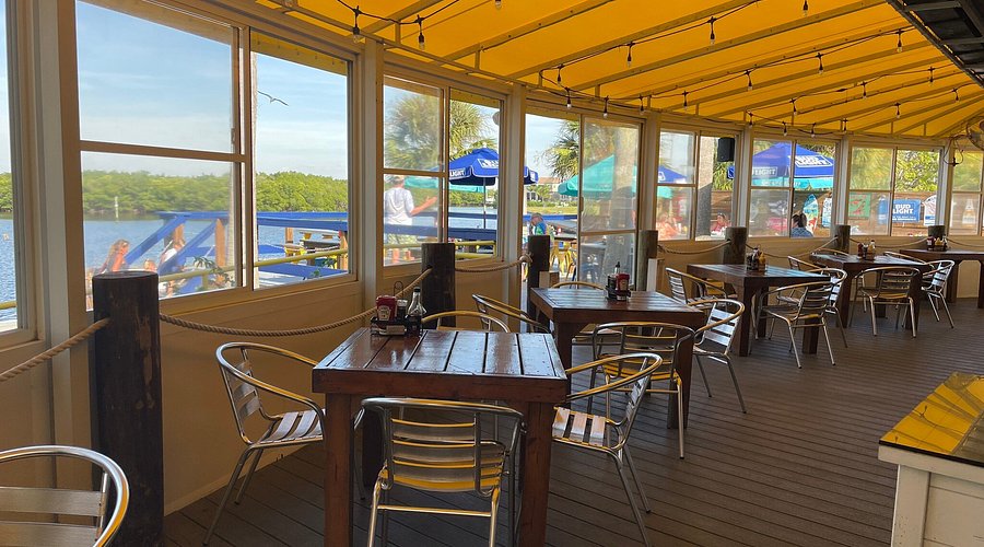 Cozy indoor seating area at a casual coastal bar, featuring wooden tables, metal chairs, and large windows with views of the water, reflecting the relaxed atmosphere of Jersey Shore beach bars.