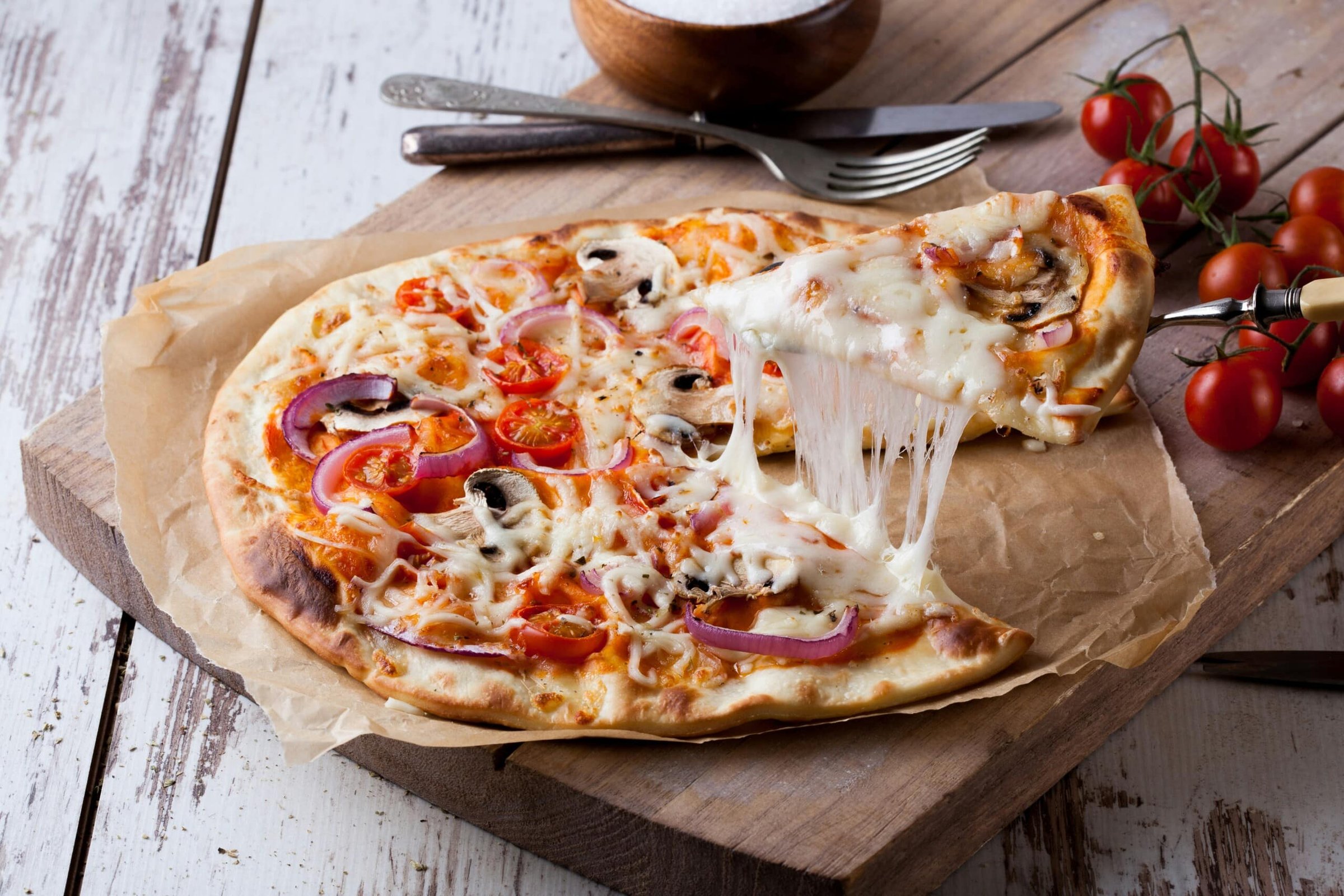 Delicious pizza with melted cheese, fresh tomatoes, mushrooms, and red onions on a wooden board, highlighting the best pizza spots in Jersey Shore.