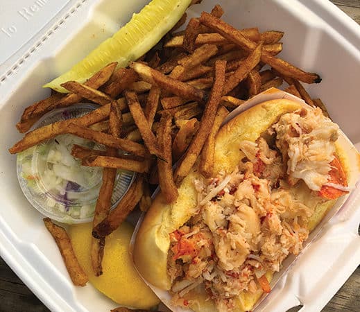 Lobster roll filled with tender lobster meat, served with golden fries and a side of coleslaw, highlighting the casual dining experience at Point Lobster in Point Pleasant Beach.